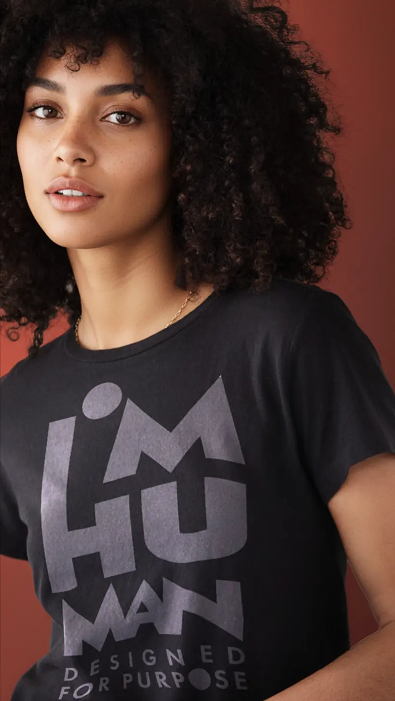 Model wearing the black I’M HUMAN tee against a clay wall